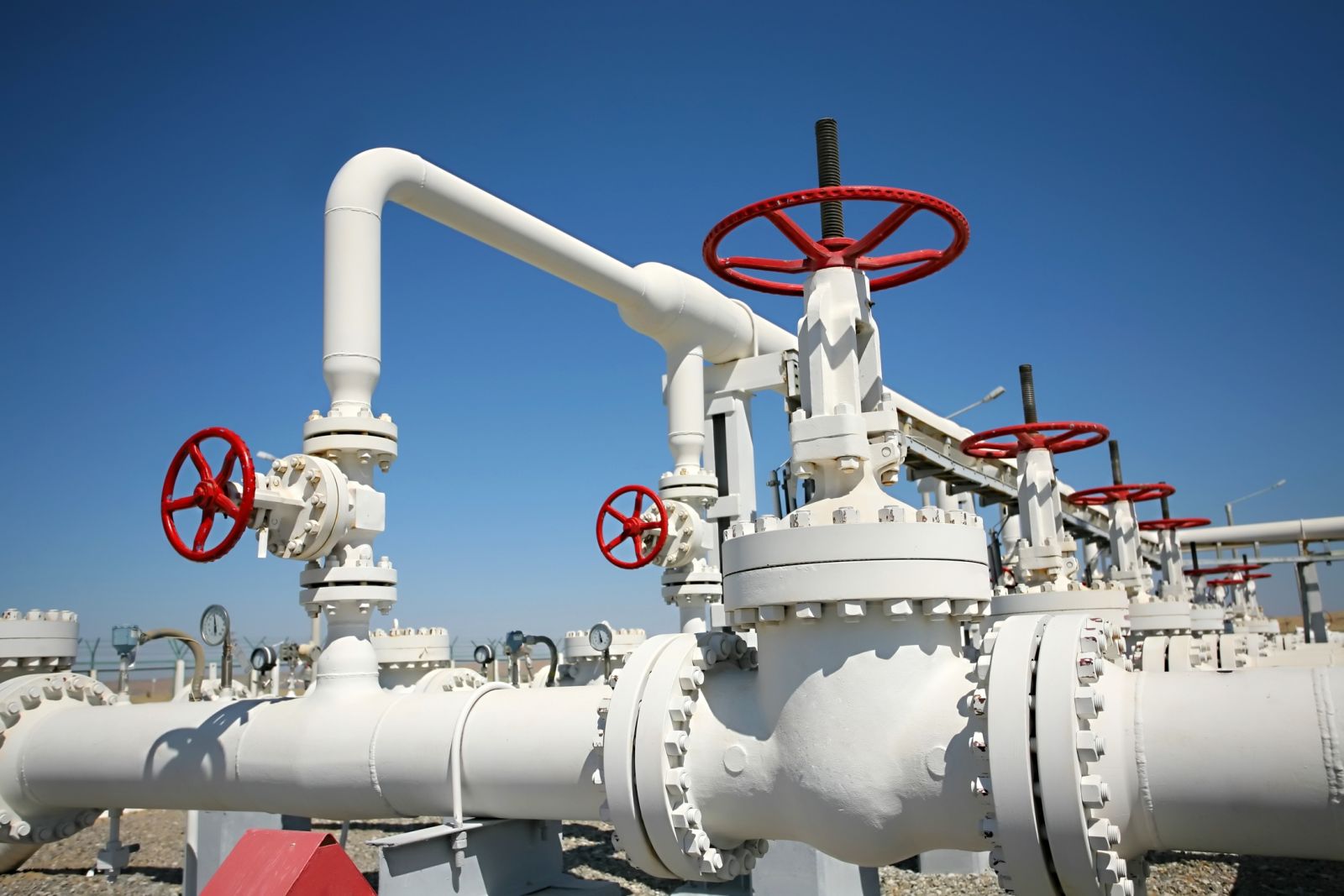 Industrial pipework and red safety valves beneath a blue sky